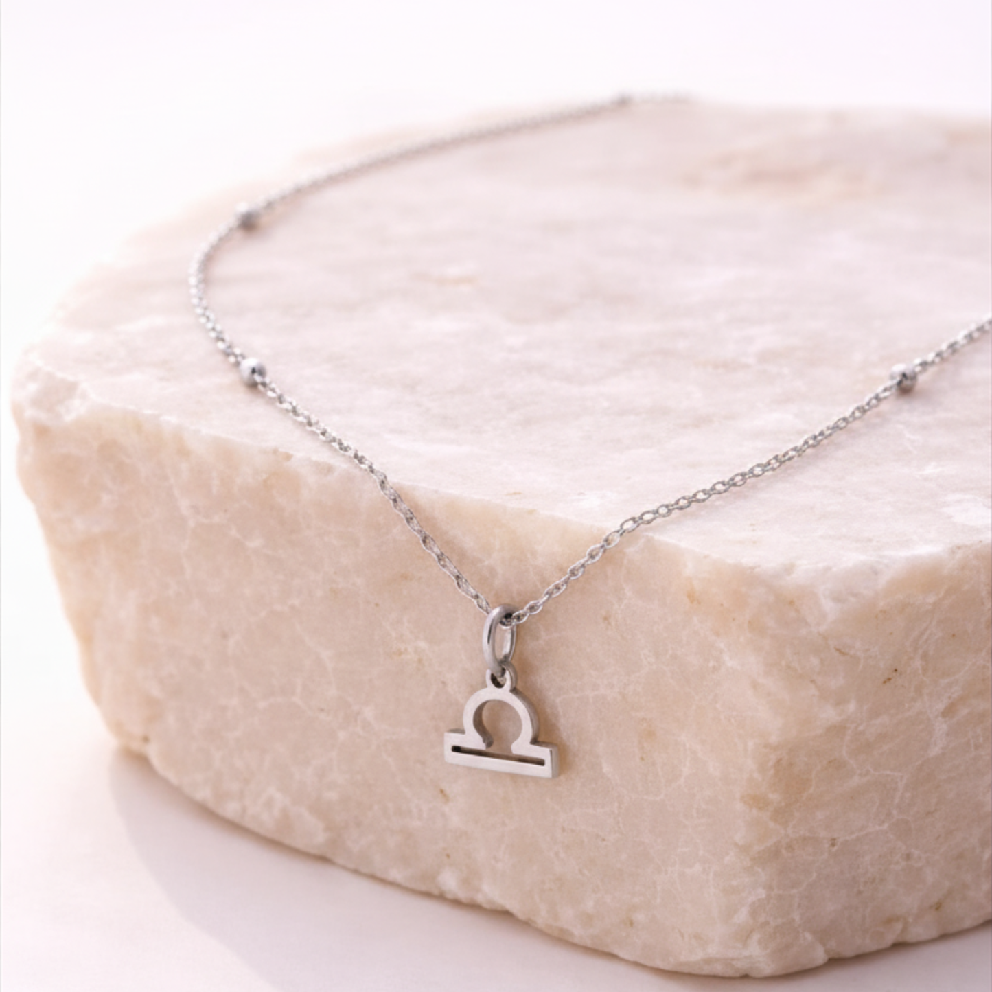 Libra zodiac necklace silver pendant on beige stone slab