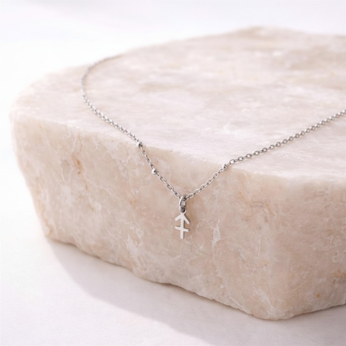 Sagittarius zodiac necklace silver pendant on beige stone slab