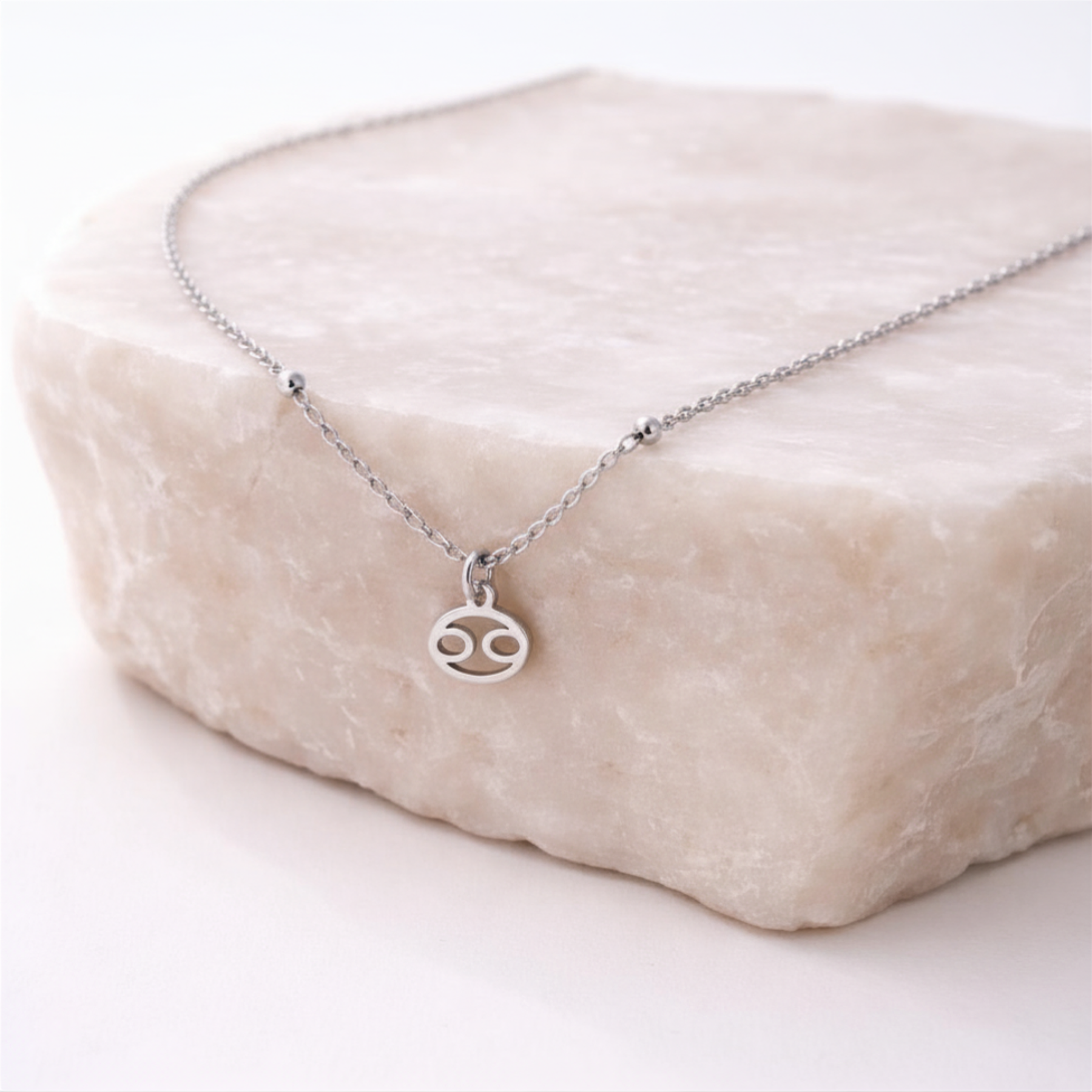 Cancer zodiac necklace silver pendant on beige stone slab