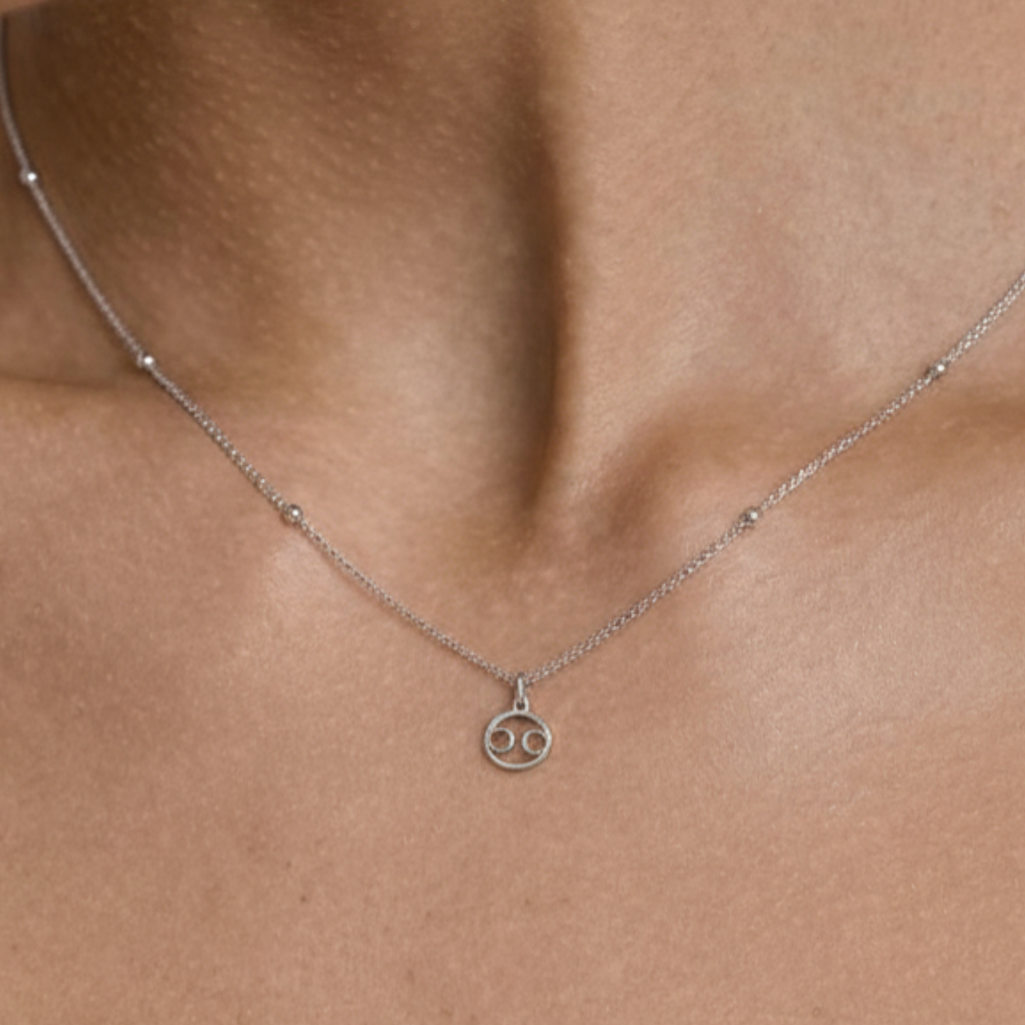 Cancer zodiac necklace silver worn on model with beige top and silver chain