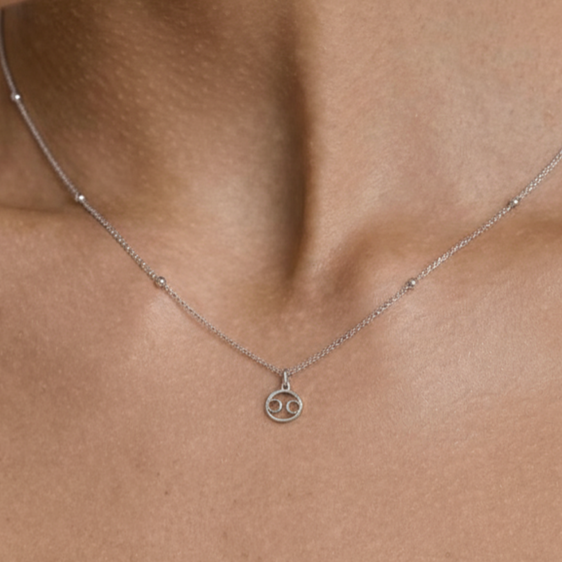 Cancer zodiac necklace silver worn on model with beige top and silver chain