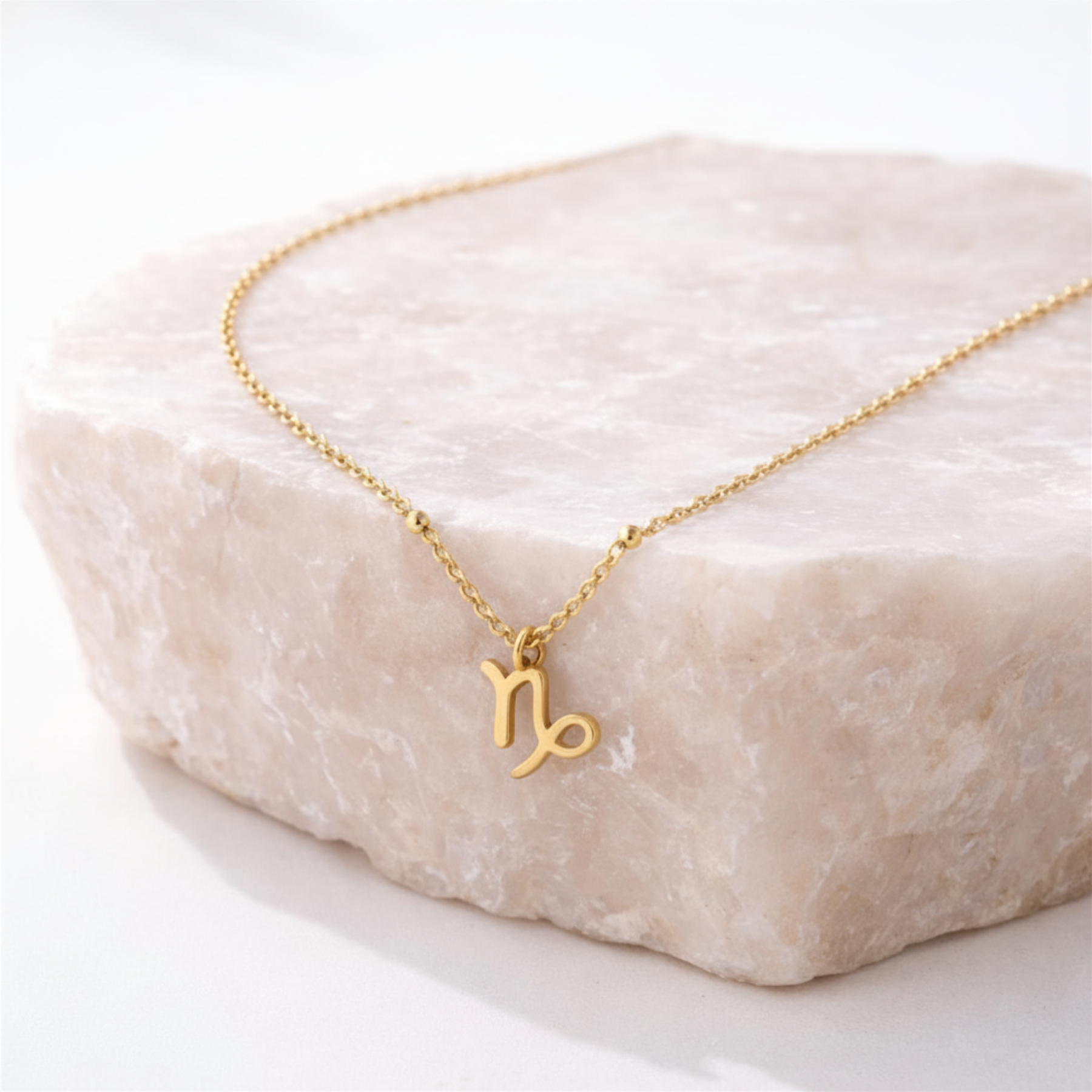 Capricorn necklace gold zodiac symbol pendant on beige stone slab