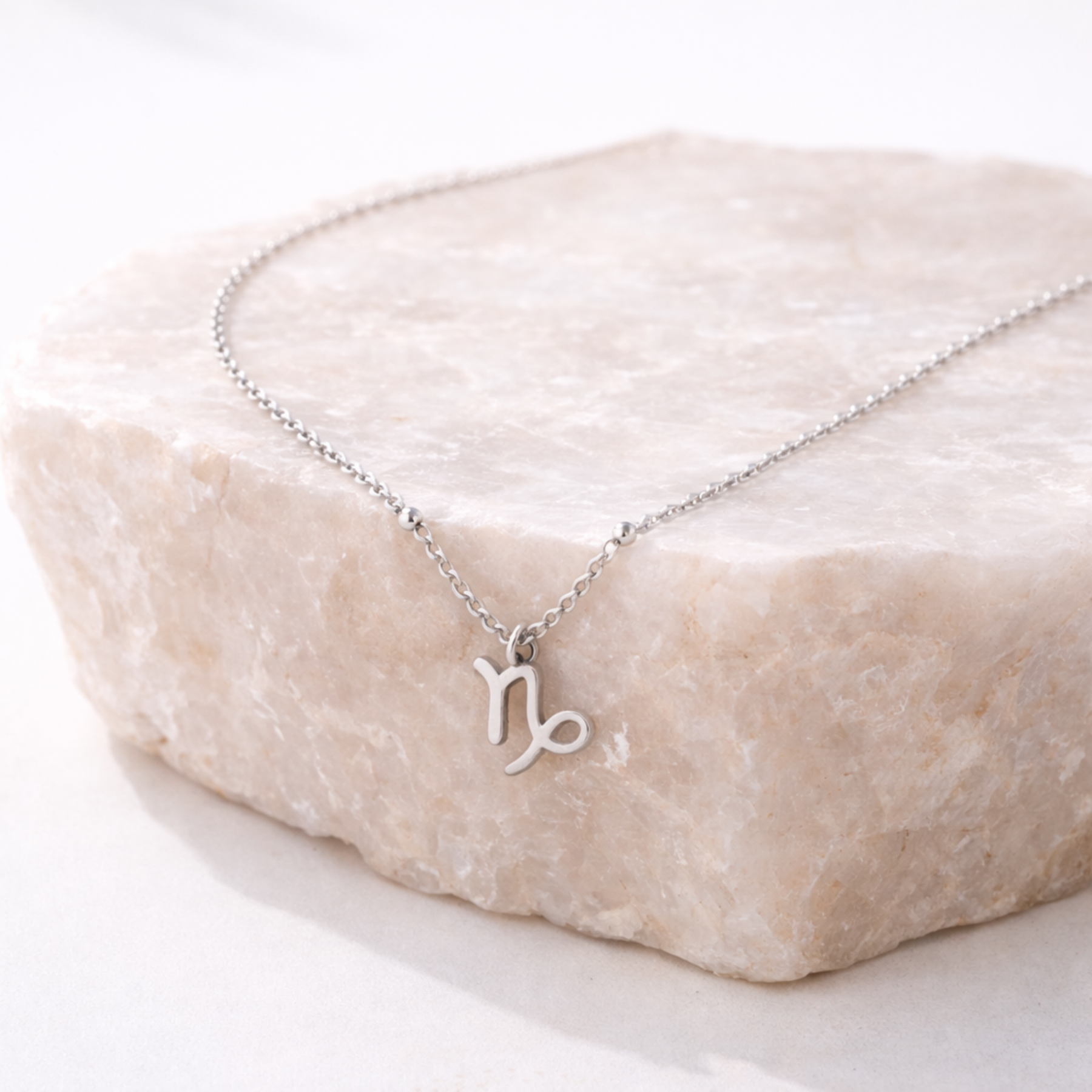 Capricorn necklace silver zodiac symbol pendant on beige stone slab