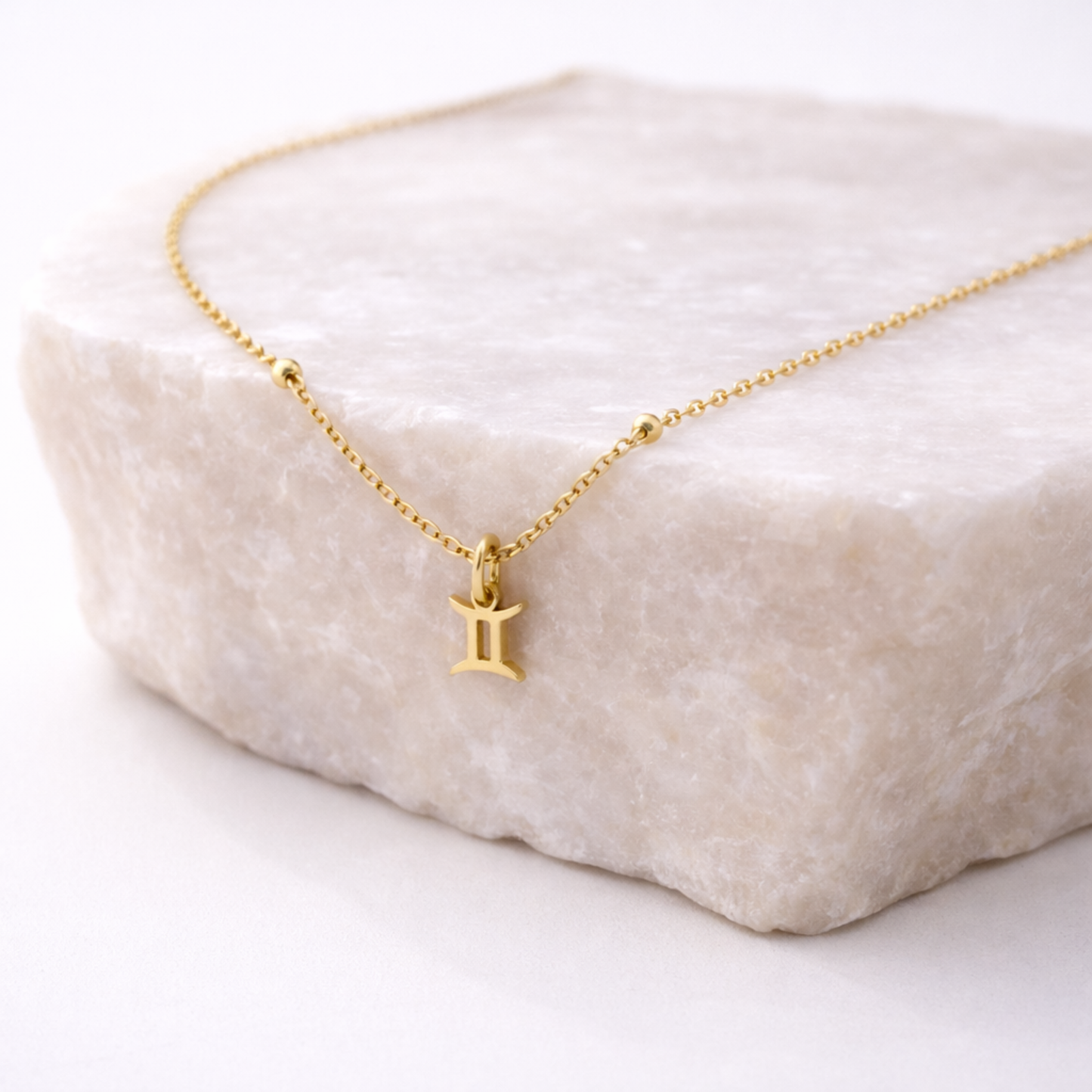 Gemini zodiac necklace gold pendant on beige stone slab