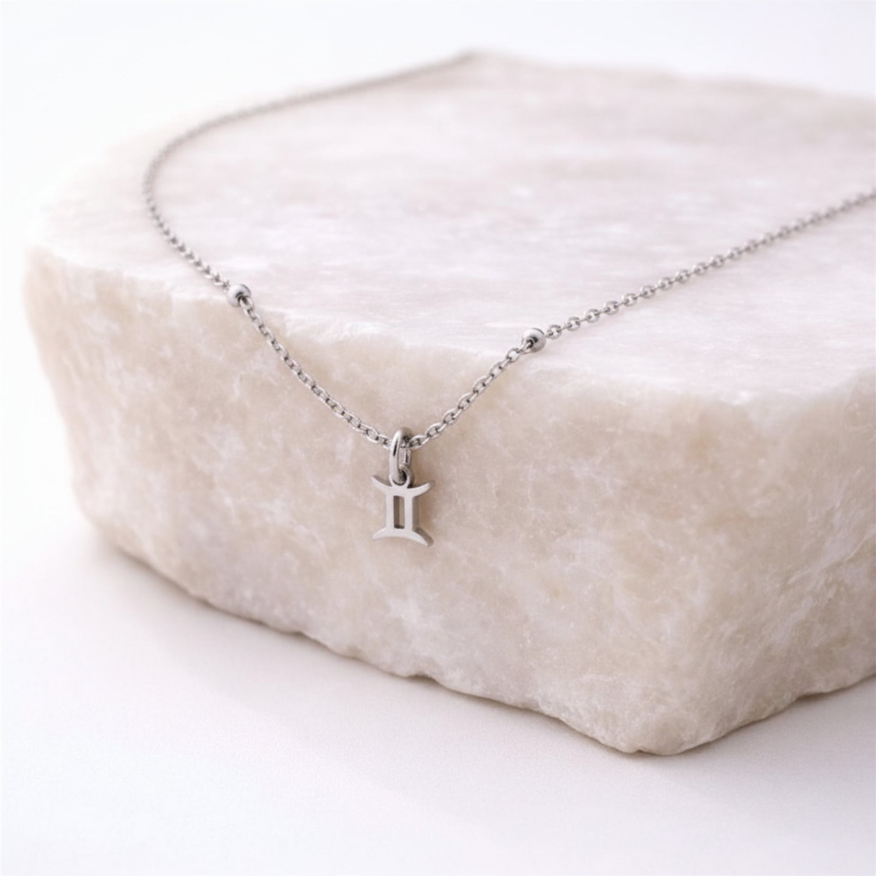 Gemini zodiac necklace silver pendant on beige stone slab