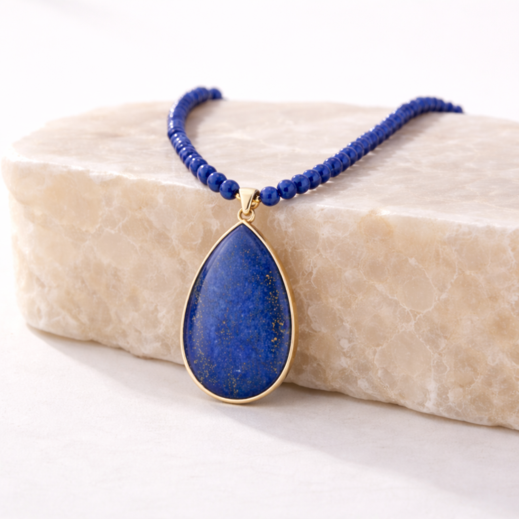 Lapis lazuli beaded necklace blue bead chain with teardrop pendant on beige stone slab