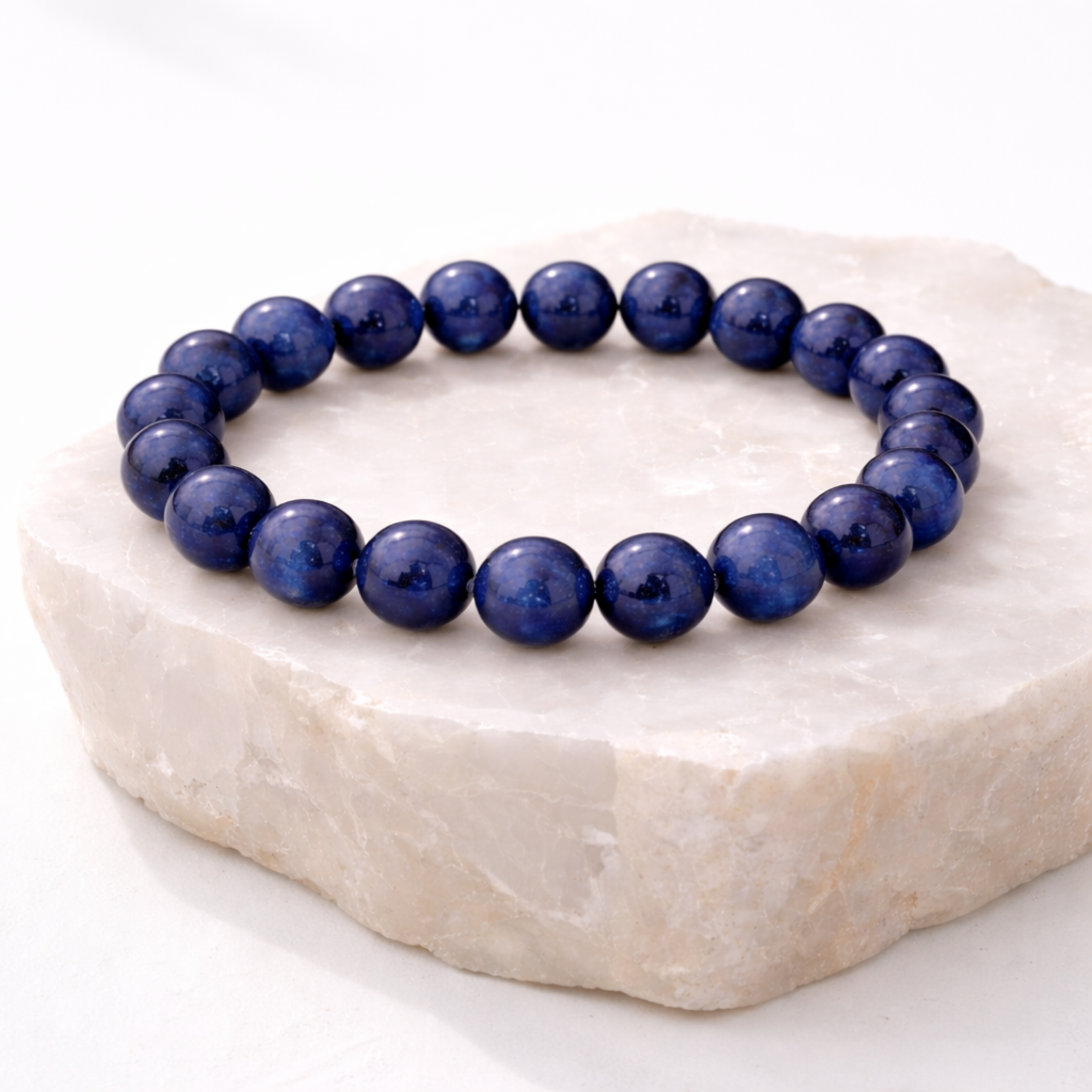 Lapis lazuli bracelet displayed on light stone slab studio product shot natural shadows