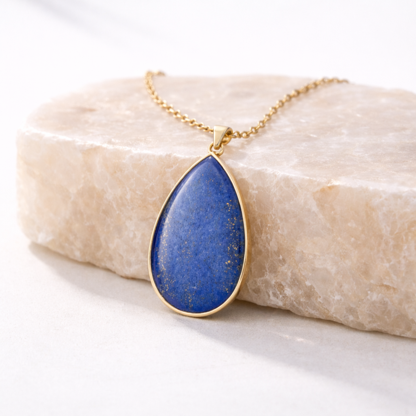 Lapis lazuli pendant necklace teardrop blue stone pendant with gold setting on beige stone slab