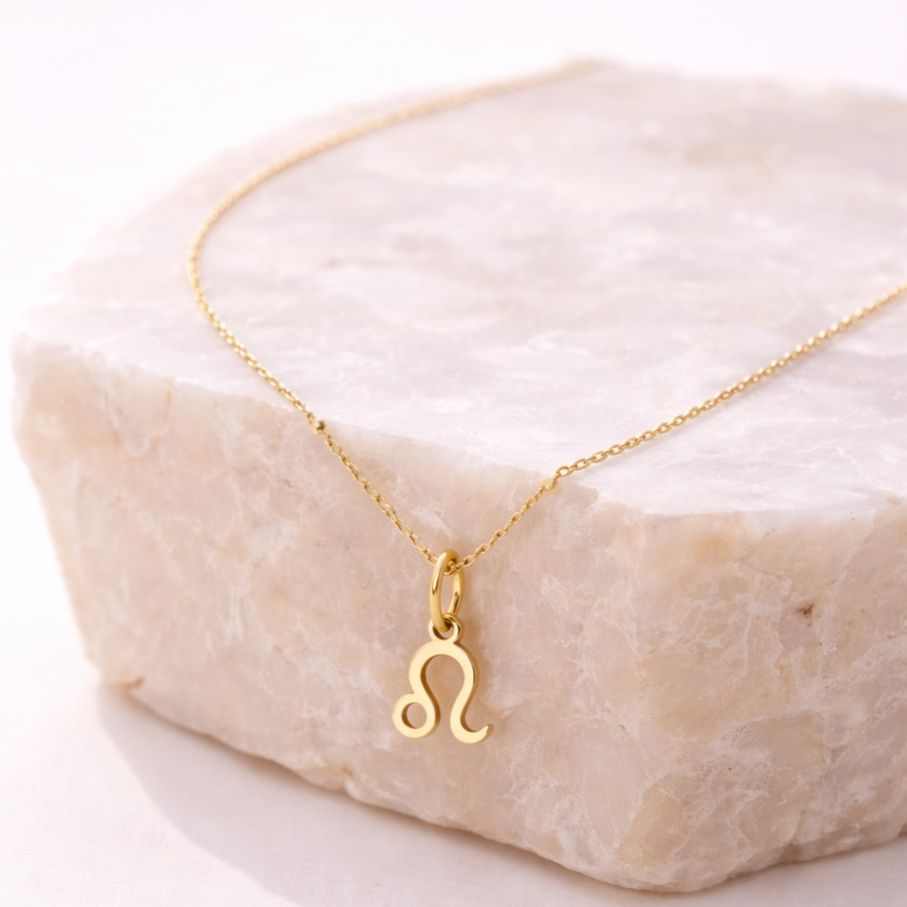 Leo zodiac necklace gold pendant on beige stone slab