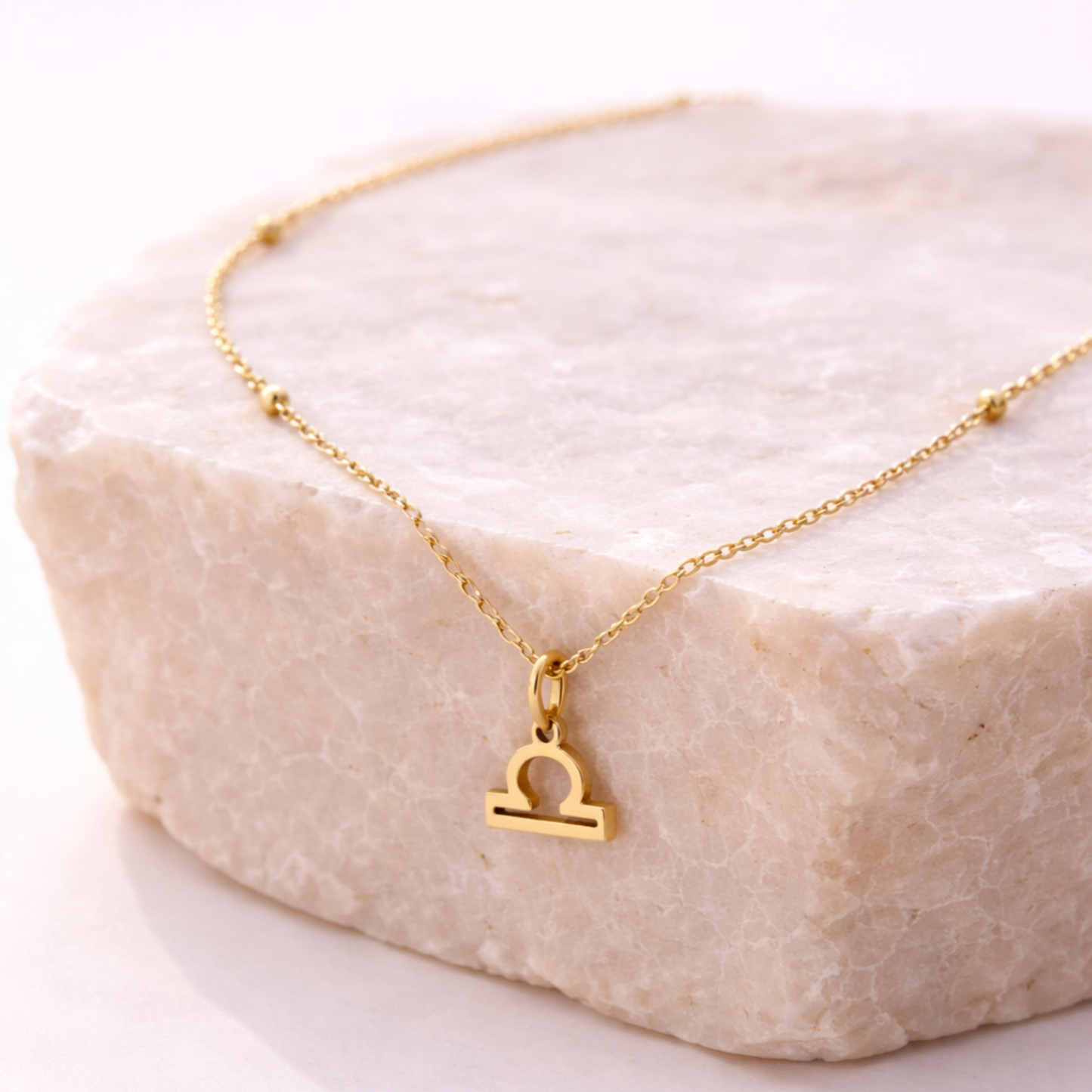 Libra zodiac necklace gold pendant on beige stone slab