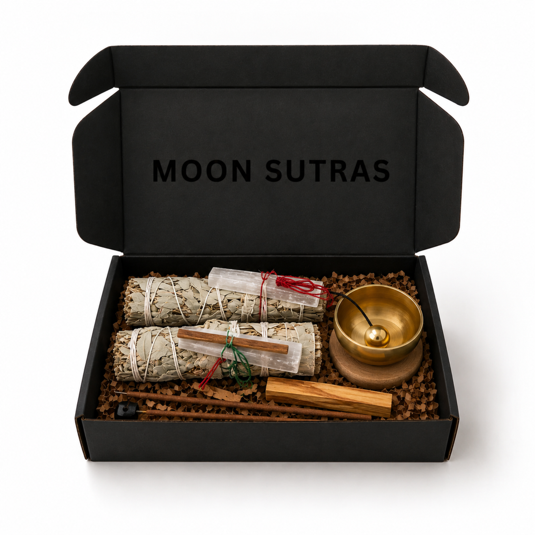 Open Moon Sutras cleansing ritual box containing two sage bundles with selenite and palo santo, a brass singing bowl and incense on a white background.