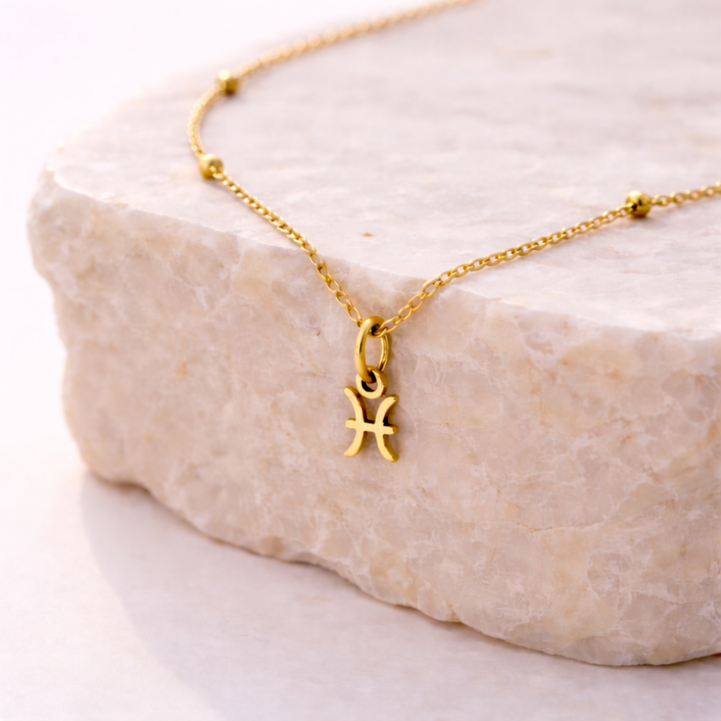 Pisces zodiac necklace gold pendant on beige stone slab