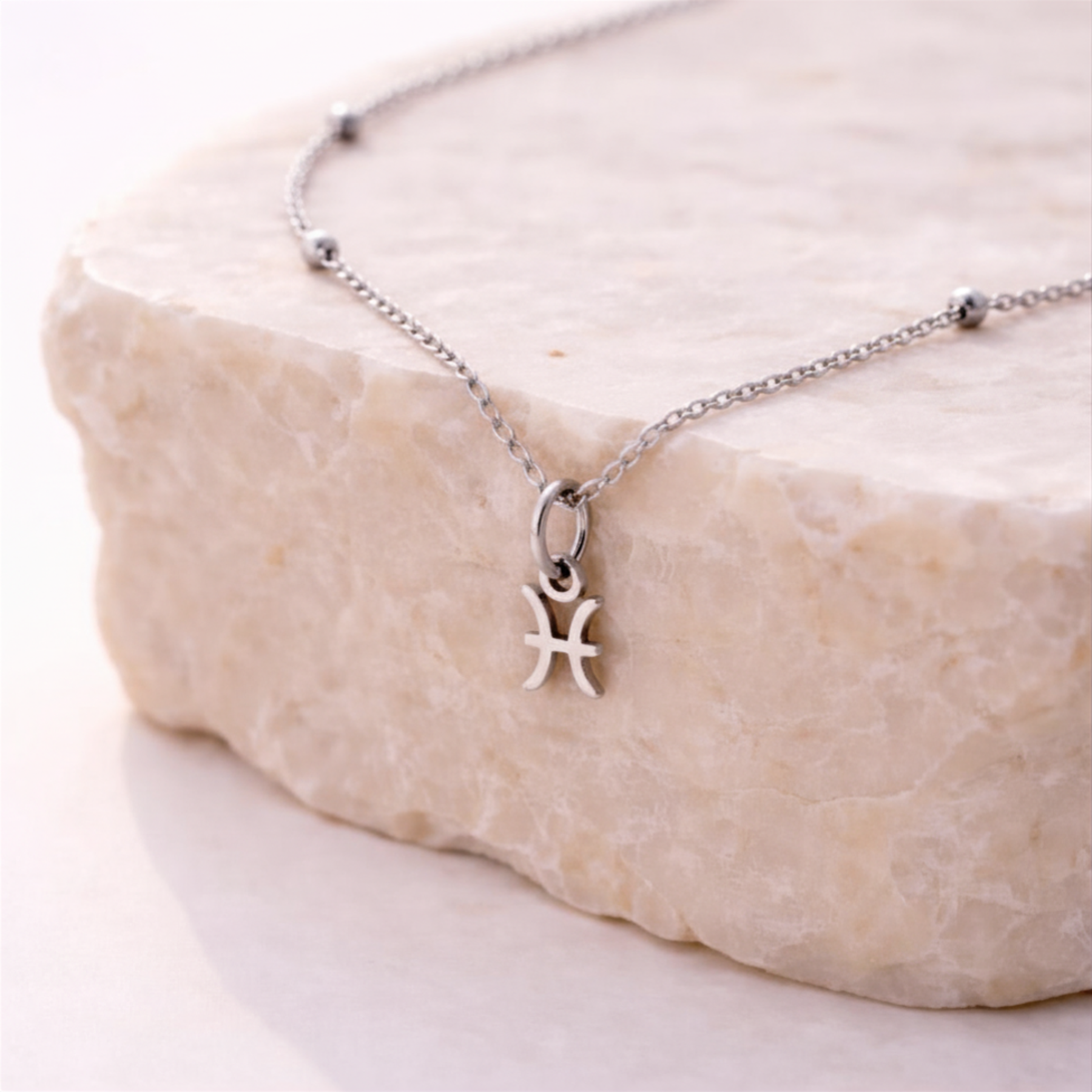 Pisces zodiac necklace silver pendant on beige stone slab