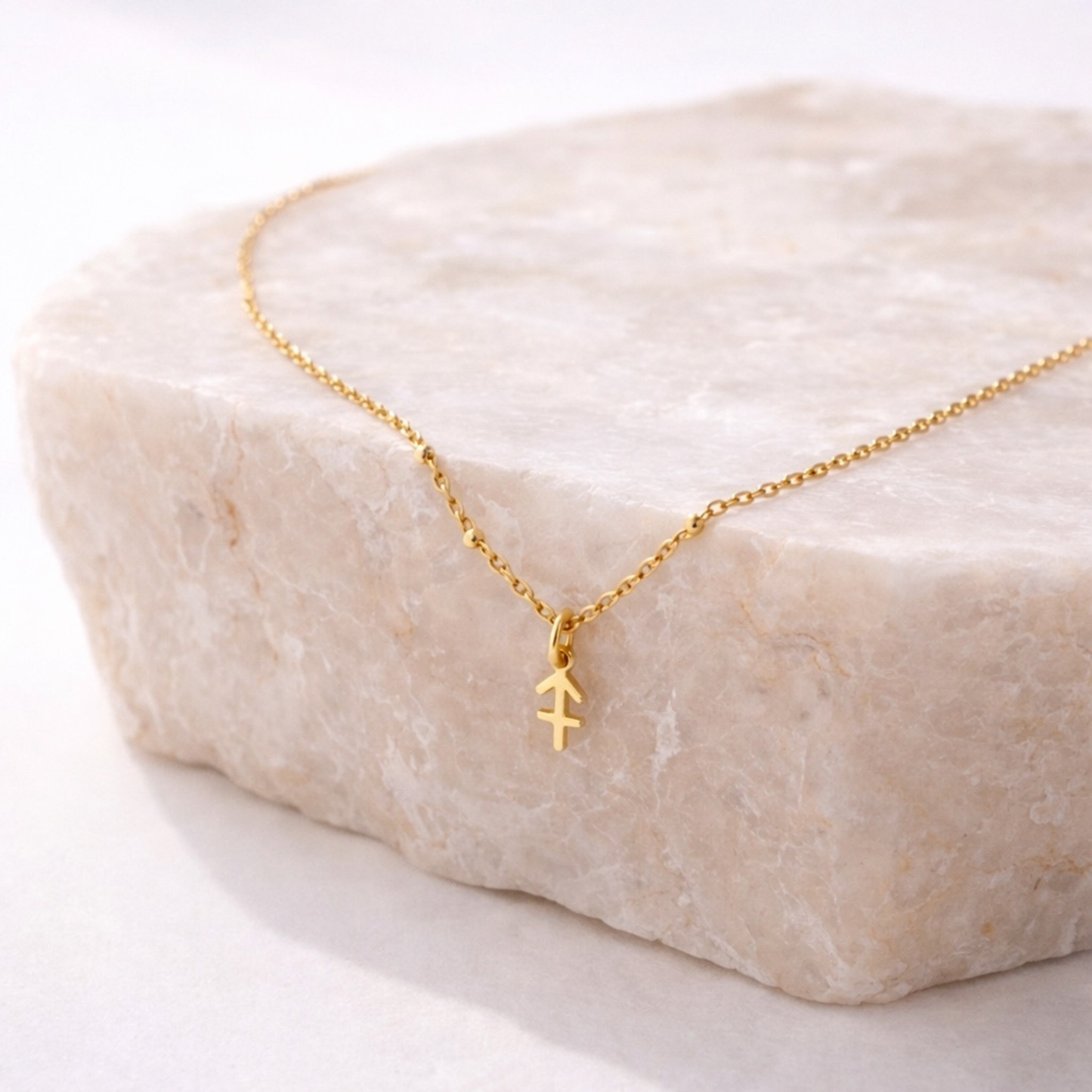 Sagittarius zodiac necklace gold pendant on beige stone slab