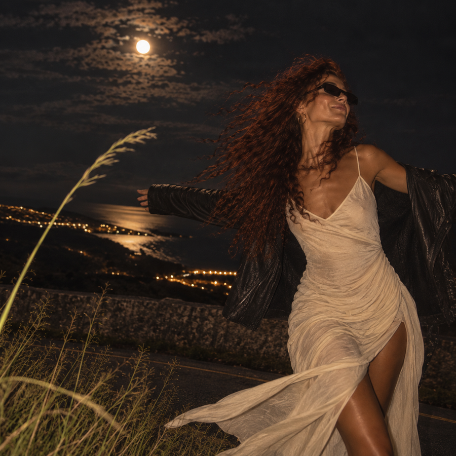 Woman standing in the wind beneath the Moon beside a bending blade of grass, representing Swati Nakshatra.