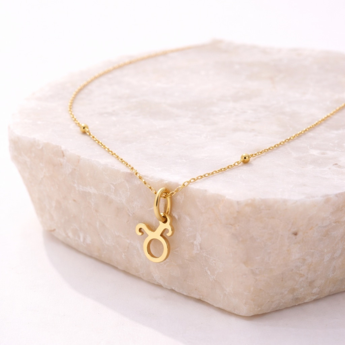 Taurus zodiac necklace gold pendant on beige stone slab